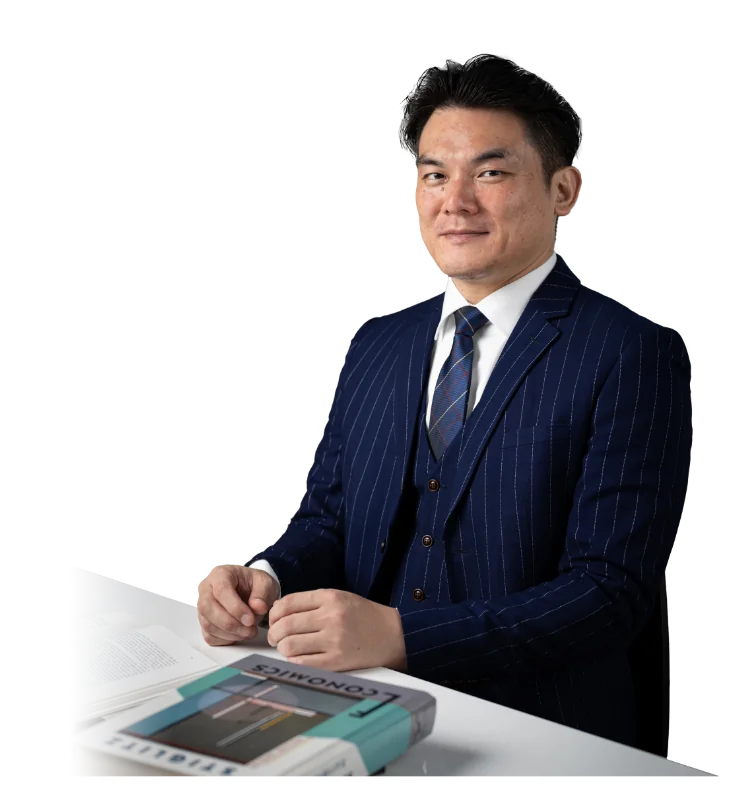 紺のストライプのスーツを着て、経済学の本を置いた机に座る原 純一